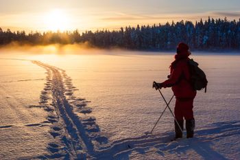 hiihtäjä järven jäällä katsomassa auringonlaskua